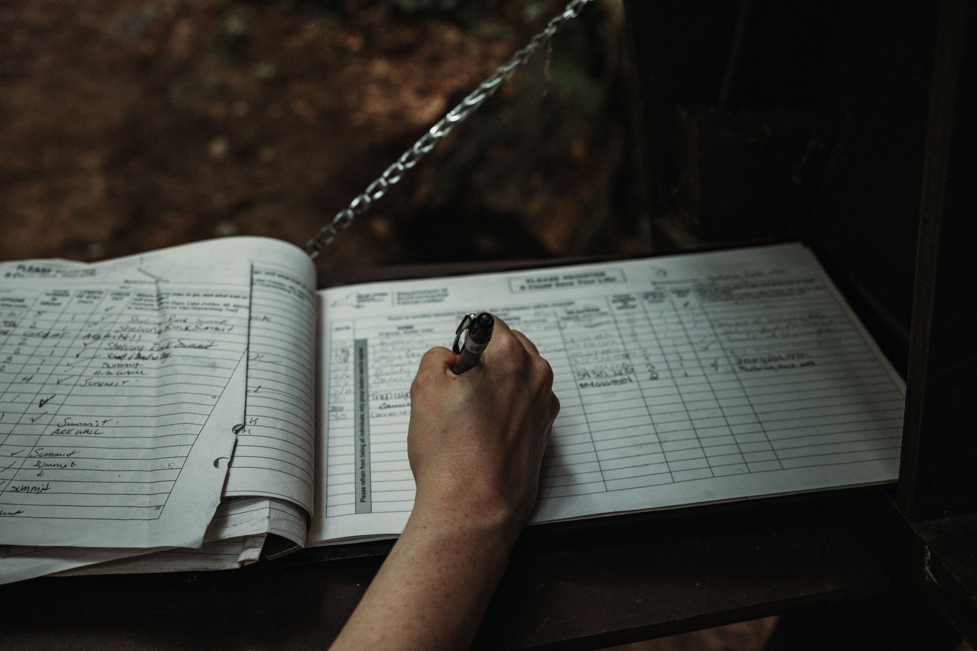 Person writing in a logbook outdoors.